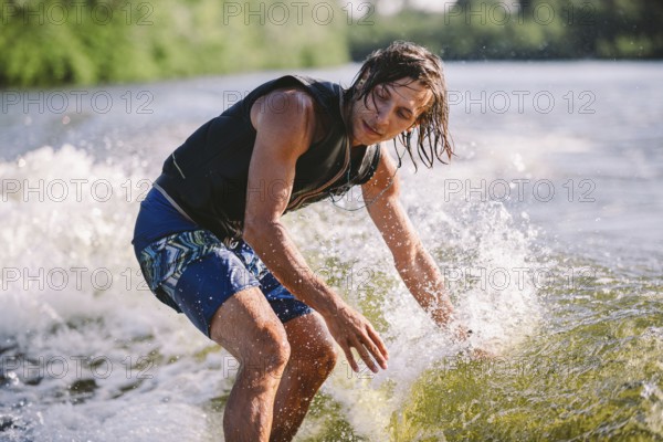 Active wakesurfer jumping on wake board down the river waves. Surfer on wave. Male athlete training on wakesurf training. Active water sports in open air on board. A man catches a wave on surf