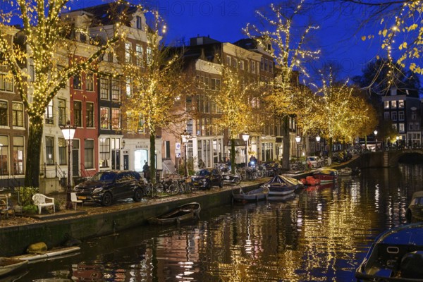 Festively decorated streets along a canal with lights and boats at night, Amsterdam, Netherlands
