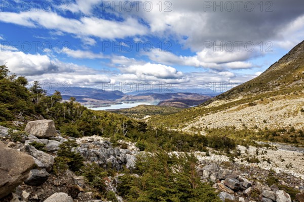 Valley with scattered rocks and views of distant hills and a shimmering blue lake, The landscape of Torres del Paine National Park in Patagonia Chile