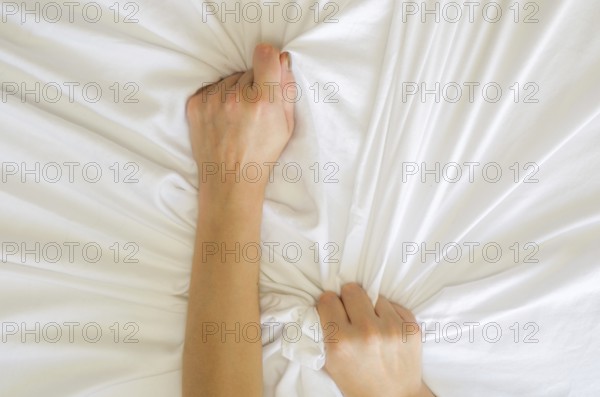 Hand sign orgasm of woman on white bed, Hand of female pulling white sheets in ecstasy, feeling and emotion concept