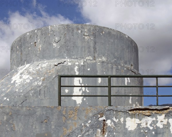 An old crumbling concrete military bunker type structure with rounded windowless surfaces and a green railing against a blue cloudy sky