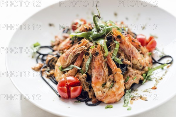 Gourmet food grilled prawn and vegetables on black squid ink pasta meal