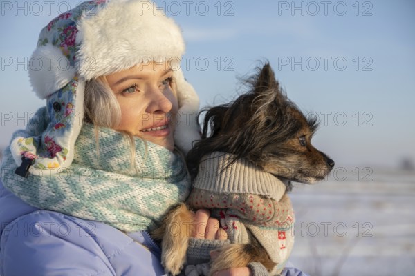 Close-up on the face of a girl looking towards the sun. The girl, wearing a cap and jacket, is outside with her dog
