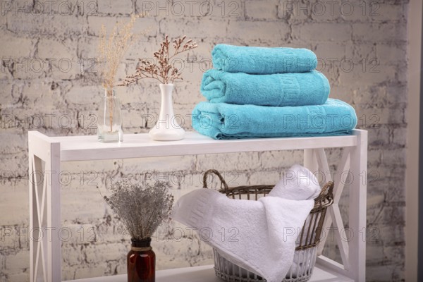 Rack with a stack of three colour turquoise towels and baskets with clean white towels and toilet decor near brick wall. Shelf with terry towels and decorative vases. Shelving unit with clean towels
