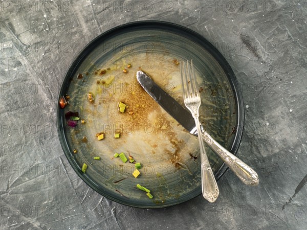 Dirty dish and silverware cutlery on gray background, top view or flat lay. Empty dirty craft plate with fork and knife on gray textured background