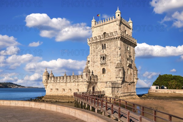 Belem tower and wooden bridge to it, Lisbon, Portugal at blue summer day sky with clouds. Medieval fort on Tagus river in late Gothic or Manueline style, UNESCO world heritage site, Age of Discoveries, tourist attraction, Portuguese seafaring history