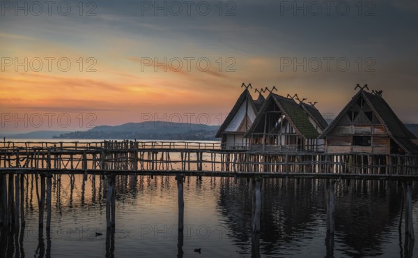 Weathered wooden cabins built on wooden pillars over the Bodensee lake water, at colorful sunset, in Unteruhldingen, Germany, Europe