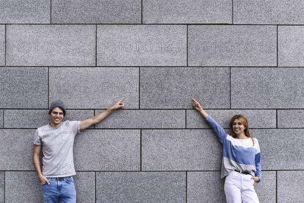 Cheerful couple at the street, show a big sale, or nice offer. Advertise concept. People, travel and tourism, on city street and couple show with their fingers something over gray wall background