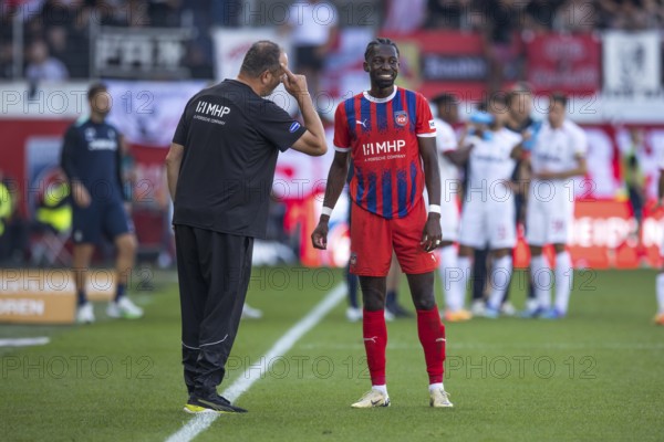 Football match, coach Frank SCHMIDT 1. FC Heidenheim left, gesturing with his right index finger to his head, giving instructions to Omar TRAORE 1. FC Heidenheim, who is visibly smiling and looking towards the pitch, Voith-Arena football stadium, Heidenheim