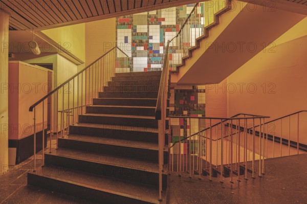 Interior with a staircase and railings, illuminated by yellowish light and with wall art, Bad am Park, Lost Place, Essen, North Rhine-Westphalia, Germany, Europe