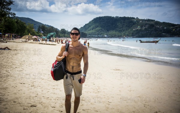 Half body shot of a handsome young man standing on a beach in Phuket Island, Thailand, shirtless wearing boxer shorts, showing muscular fit body, Asia