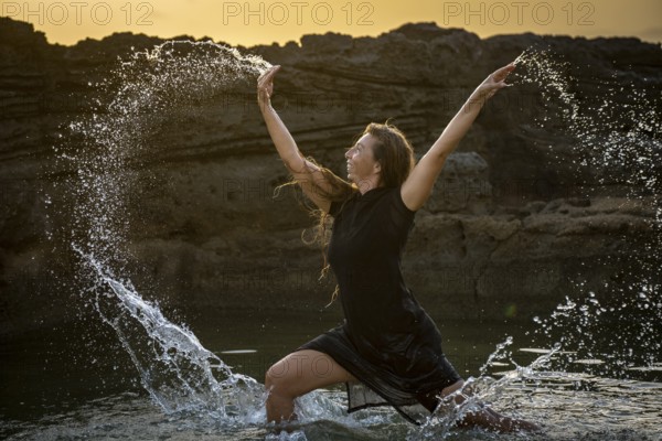 Middle-aged woman dancing and throwing water in the air, Maioris beach, llucmajor, Majorca, Balearic Islands, Spain, Europe