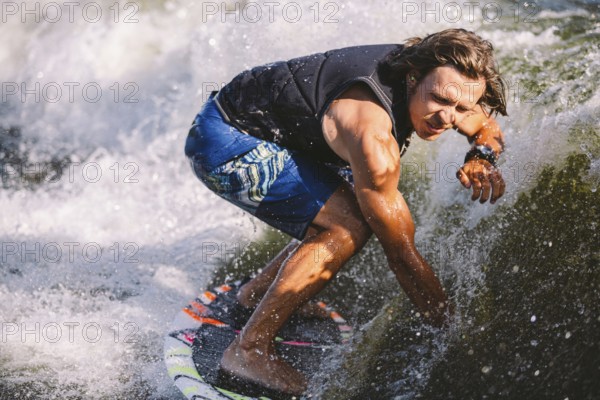 Young athletic man with long hair wakesurfing on waves of river in sunny summer weather. Ttheme outdoor activities in summer. Water sports wakesurf on the board. sliding wakeboarder in water splash