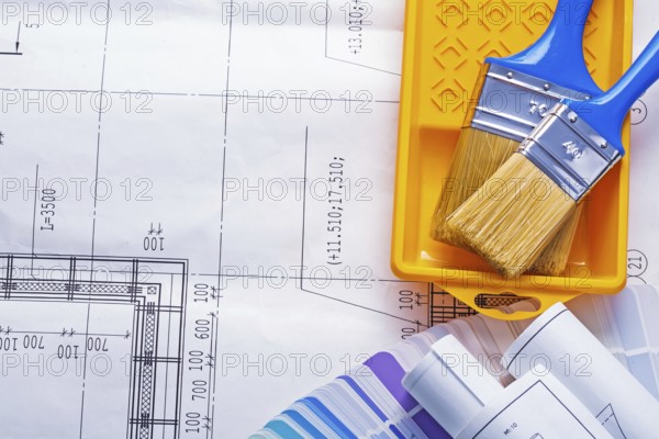 Two paintbrushes in paint can with rolled blueprints on color sampler with copyspace