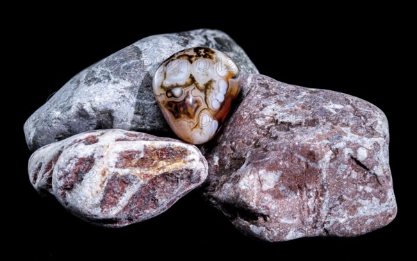 A smooth, polished agate gemstone with intricate banding patterns rests on a group of textured, multicolored rocks against a black background. The image highlights the contrast between the stones glossy surface and the rough texture of the rocks, Odessa, Ukraine, Europe