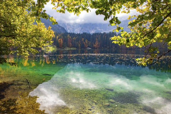 Picturesque lake Fusine in Northern Italy. The bright colors of the autumn forests are reflected in the icy water of the lake. Yellow, orange and red leaves are illuminated by the sun