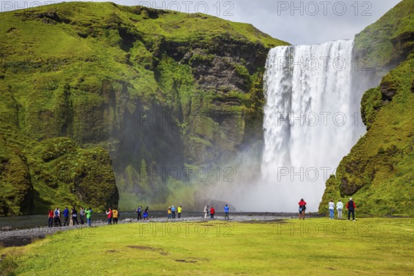 Magnificent famous waterfall Skógafoss, Iceland. A powerful jet Skógar river falls from a large glacier. Tourists delighted the crowd at the foot of roaring jets