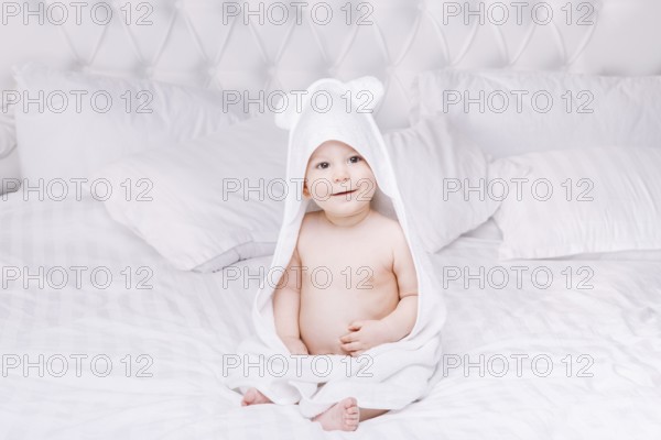 Adorable newborn baby boy with brown eyes sitting wrapped in a white towel with ears in light bed. A happy childhood and the concept of health. Joyful, happy, emotional. beautiful baby