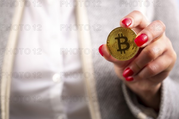 Virtual cryptocurrency money Bitcoin golden coin in the left hand of a woman with red nail polish. The future of money