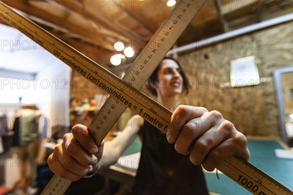 A closeup view of two wood measuring rods being held by a woman tailor inside her retro studio. Artist shows tools used in design process