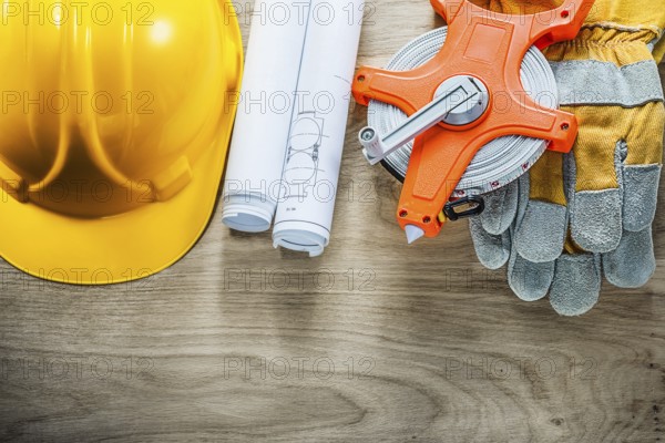 Rolled blueprints protective gloves tape measure hard hat on wooden board