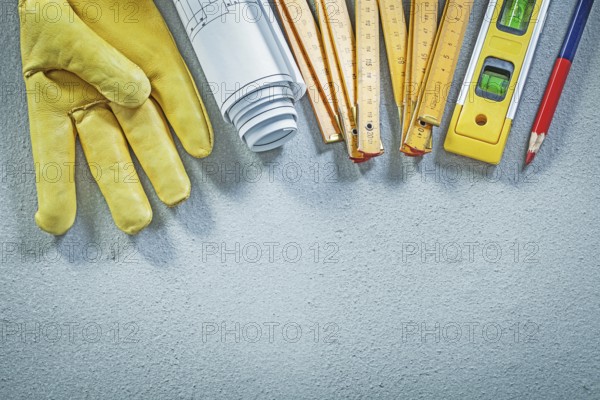 Protective gloves construction level wooden meter blueprints pencil on concrete background building concept