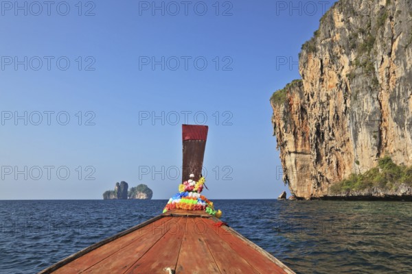 The Thai excursion boat floats to ocean island. The boat nose is decorated by multi-colored and bright silk scarfs