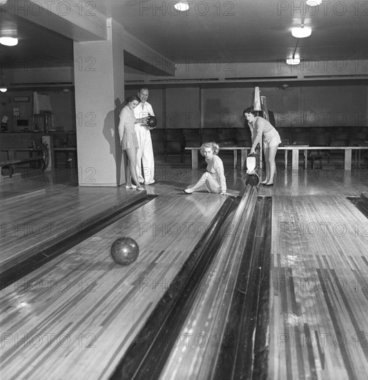 Bowling in the 1950s. A man with three young women in a bowling alley. They are dressed in short striped skirts and jumpers. The three girls are all theatre actresses, Ingrid Björk, UllaCarin Rydén and Brita Ulfberg. Ewert Ekström shows is instructing them in bowling. He was a professional bowler player in the 1930s and is at this time an instructor and owner of the bowling club. 1950. Sweden Kristoffersson ref AY35-7
