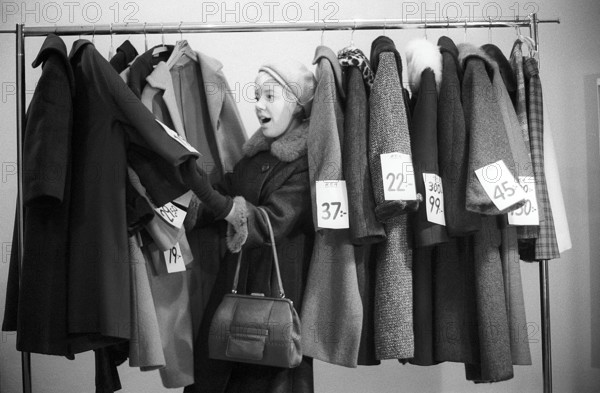 Great discounts of outerwear in the 1960s. A woman stands by a clothes rack, choosing from outerwear and coats marked with price tags with discounted prices. Judging by her face, she appreciates the reduced prices and thinks she's getting real bargains. Sweden January 1963. Ref CV28
