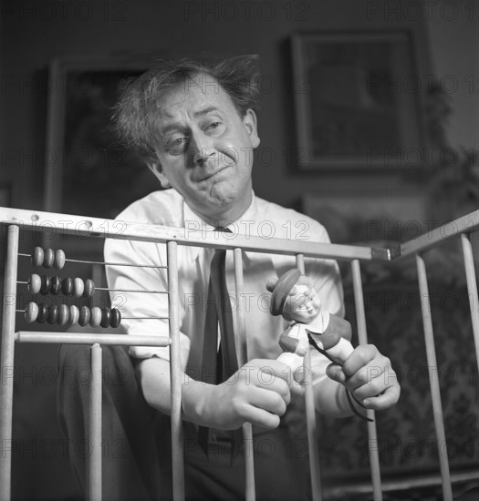 Father in the 1940s. Actor Åke Söderblom, 1910-1965 tries his best at amusing his son from outside the playpen playing with a a doll. Judging by the look on his face he has no success in cheering up his son. Sweden 1949 AN93-3