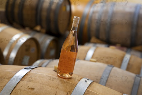 A bottle of rose wine on Oak Barrels wine fermenters in a winery