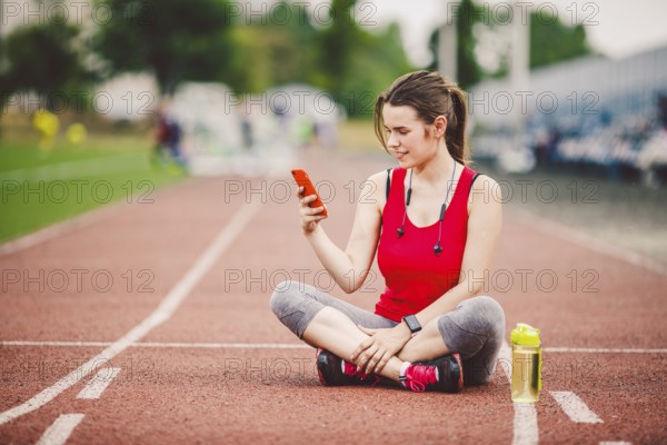 Beautiful fitneß girl uses smartphone at stadium after workout. Sports and healthy. Sport woman use of cellphone inside sport complex. Sport and technology. resting after workout, run at red track