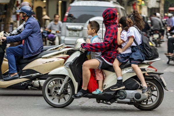 A person with children on a motorbike in a busy city street, woman with children on a scooter in the traffic of Hanoi Vietnam