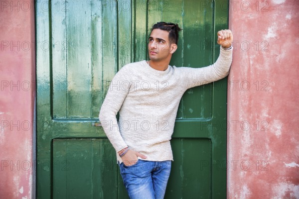 Elegant young man leaning against old wall and green door