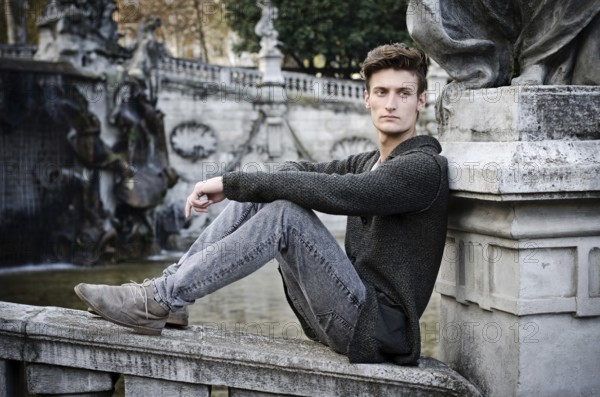 Handsome young man outdoors, sitting on old stone balusters looking away