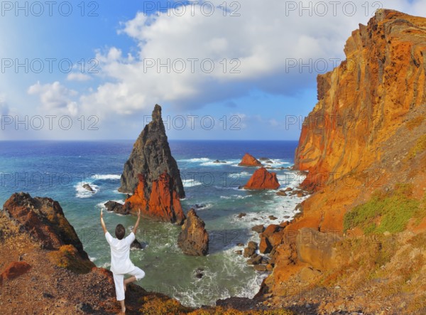 The woman ashore in a white suit for yoga carries out a pose Tree. Atlantic storms. Colorful pinnacles lit sunset. Arid eastern tip of the island of Madeira