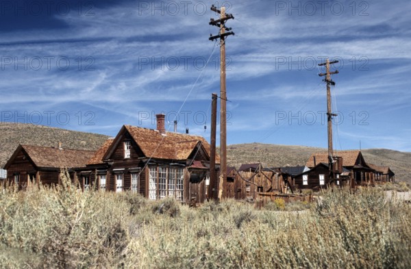 Ghost town of Bodie: Windswept wooden houses, lamp posts and a sweeping view of the surrounding prairie hills. Colour photo, landscape format