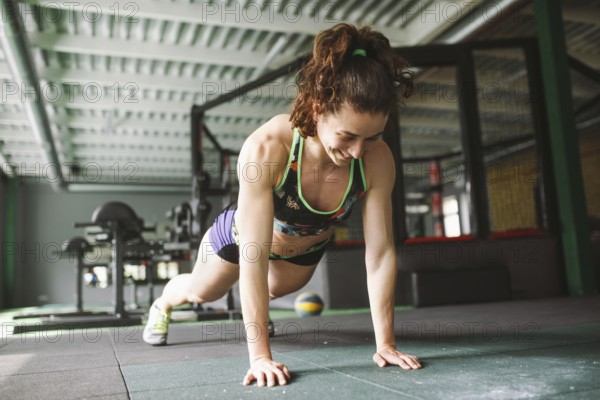 The girl does push-ups from the floor in the gym. Training muscles of the back, arms and press. Working with your weight