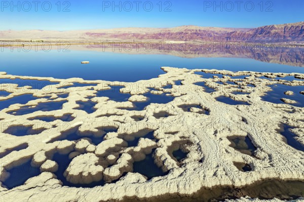 Dead Sea. Evaporated salt forms bizarre patterns on the water. Sunny winter day. The blue water is surrounded by pink mountains. The picture was taken by a drone from a aerial view. Israel