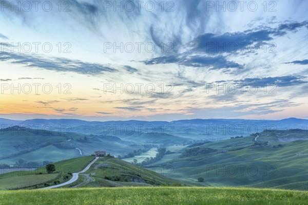 Italian valley in the dawn light with a farm on a hill