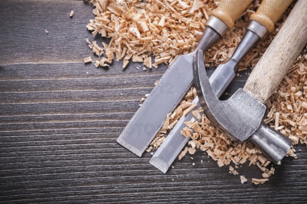 Close up of joiner's hammer and metal firmer chisels in wooden planning chips on vintage wood board construction concept