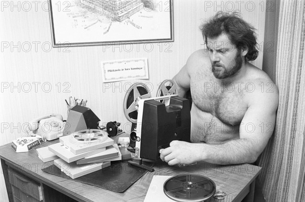 Film projector in the 19702. Ricky Bruch (1946-2011) Swedish track and field athlete. He competed in the discus and shot put sports. He is seen with a film projcector. The film was usually shown on a white screen. The front roll on the projector contains the film ready to be seen, the back roll is the film rolled up as it is viewed. Once the film is finished, the back roll containing the film was rolled back onto the original roll. Sweden 1975