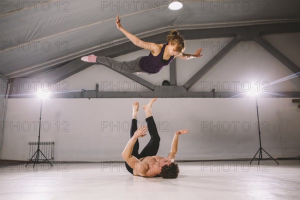Young couple Couple practicing acro yoga in gym. Healthy lifestyle. Acroyoga. Couple yoga. Partner yoga. Muscular man throwing women to air. Concept of trust, strength and courage