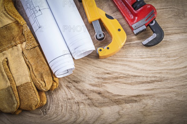 Blueprints protective gloves pipe wrench cutter on wooden board plumbing concept