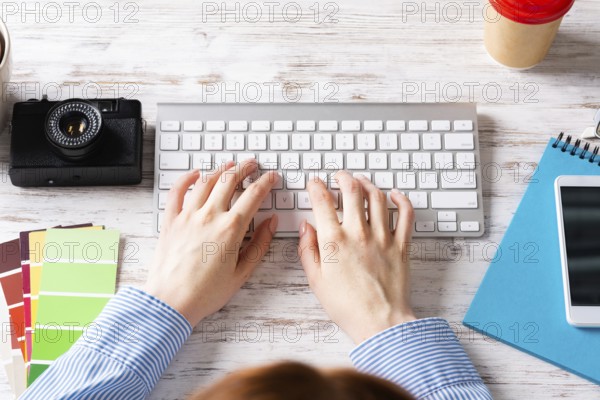 Freelancer sitting at desk and typing on keyboard. Business occupation and innovation. Office workplace with camera, notebook and disposable cup of coffee. Woman blogger work at wooden desk