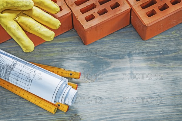 Red bricks leather working gloves construction plans wooden meter on wood board bricklaying concept