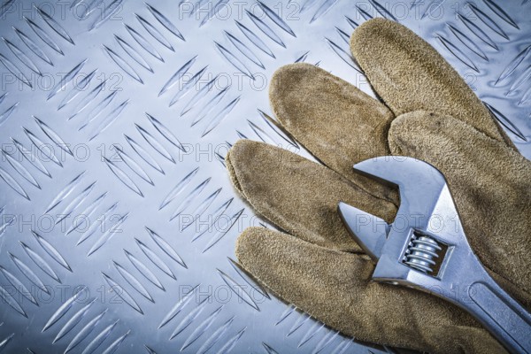 Safety gloves adjustable wrench on grooved metal plate construction concept
