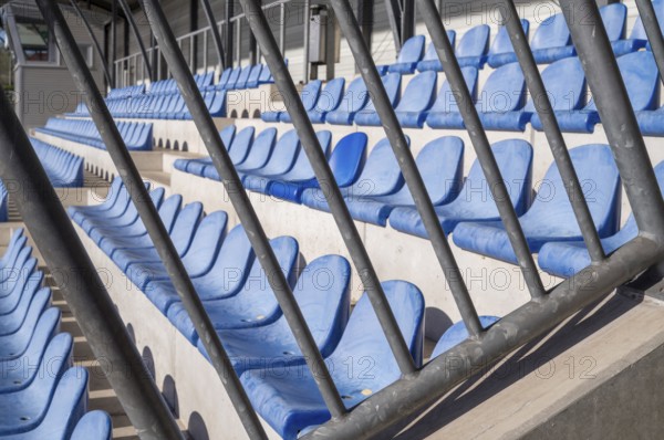 Rows of empty blue plastic stadium seats behind a metal barrier await the return of fans