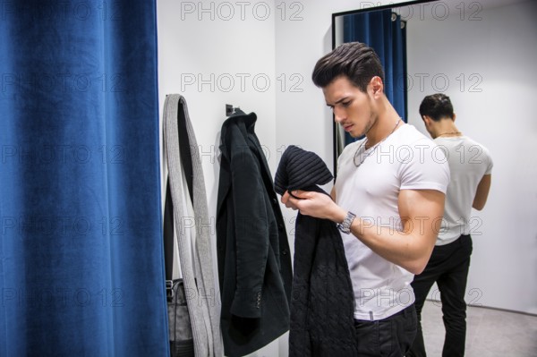 Young Handsome Man Trying on Clothes in Clothing Store&#39, s Changing Room in Front of a Mirror or in Room Closet