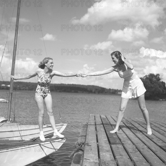 1940s summer. Two young at a marina on a summer's day. The girl getting from the boat onto the bridge needs a helping hand. Photo Kristoffersson ref P13-5. Sweden 1945